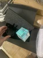 Lâmpada de plasma com base de vidro transparente, conectada a um suporte preto, dentro de uma caixa de embalagem.