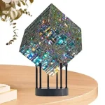 Cubo de cristal decorativo com efeito de prisma, apoiado numa base preta com quatro suportes finos, colocado numa mesa de madeira clara.