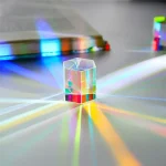Pequeno cristal prismático transparente com efeito de dispersão de luz, refletindo cores do arco-íris na superfície plana.