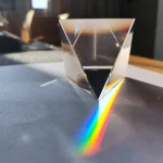 Prisma de vidro transparente projetando um espectro de cores no papel, com foco na reflexão e dispersão da luz.