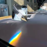 Cubo de prisma de vidro transparente refletindo luz, criando um espectro de cores na superfície.