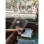 Lâmpada de plasma pequena, visível através de embalagem de plástico transparente, com fundo de janela e rua ao ar livre.