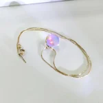 Colar com corrente dourada e bola de luz LED que emite cores multicoloridas, visto de cima sobre fundo branco.