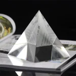 Pirâmide de espelho com faces triangulares refletindo luz, colocada sobre uma revista aberta, fundo preto.