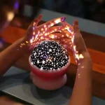 Lâmpada de plasma com padrão de estrelas e luzes coloridas, mãos a segurar a lâmpada, ambiente escuro, efeito de luzes cintilantes e brilho.