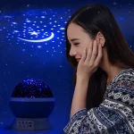 Lâmpada de projeção de estrelas com céu estrelado e lua, iluminando o quarto com luz azul, vista de perfil de uma jovem a apreciar a luz.