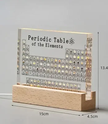 Tabela periódica de elementos em acrílico transparente com base de madeira, mostrando detalhes dos elementos químicos e suas posições.