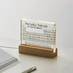 Tabela periódica de elementos em miniatura colocada numa base de madeira, com detalhes visíveis dos elementos químicos e símbolos.