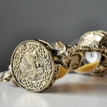 Detalhe de uma pulseira de metal com medalhão de dragão, mostrando detalhes intricados e acabamento dourado envelhecido.