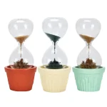 Três relógios de areia decorativos com plantas em diferentes cores de vasos: vermelho, creme e verde, cada um com plantas diferentes na base de areia.