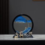 Ampulheta decorativa com base de metal, vidro transparente e areia azul, vista frontal em ambiente moderno.