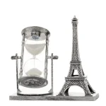 Relógio de areia antigo com estrutura de metal e miniatura da Torre Eiffel ao lado, ambos em uma base de madeira.