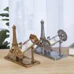 Dois relógios de areia decorativos, um dourado e um prateado, com detalhes da Torre Eiffel, colocados numa mesa de madeira junto a um computador portátil e uma planta.