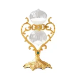 Relógio de areia decorativo com estrutura dourada e detalhes ornamentais, contendo dois recipientes de vidro com areia branca, em fundo branco.