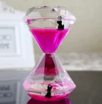 Relógio de areia de vidro com areia rosa, decorado com pequenos pinguins de plástico na parte superior e inferior.