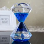 Relógio de areia decorativo feito de cristal com água azul no interior, com detalhes brilhantes e uma base sólida.
