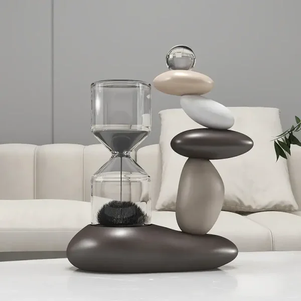Escultura moderna composta por pedras de diferentes tamanhos e cores, com um elemento de vidro transparente no topo, colocada numa mesa branca.