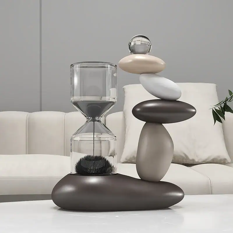 Escultura moderna composta por pedras de diferentes tamanhos e cores, com um elemento de vidro transparente no topo, colocada numa mesa branca.
