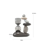 Arranjo de pedras de diferentes tamanhos e cores com um elemento de vidro transparente no topo, sobre uma base de pedra escura, medindo 22,5cm de altura.
