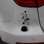 Adesivo preto e branco de um frasco de laboratório com elementos químicos e átomos ao redor, aplicado na parte traseira de um carro branco.