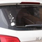 Adesivo de laboratório com tubo de ensaio, flores e bolhas, colado na parte inferior do vidro traseiro de um carro branco.