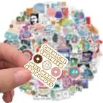 Mão segura adesivo com donuts e texto, fundo cheio de outros adesivos coloridos relacionados com ciência e gadgets educativos.