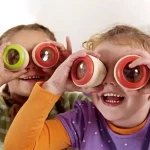 Duas crianças sorridentes usando óculos de observação coloridos, explorando o mundo com curiosidade e entusiasmo, em um contexto educativo e lúdico.