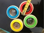 Quatro lentes de observação com molduras coloridas (azul, vermelho, verde, amarelo) e uma régua de medição, colocadas sobre uma superfície escura.