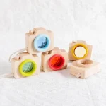 Conjunto de câmeras de brinquedo de madeira com lentes coloridas em azul, amarelo, verde e vermelho, em diferentes ângulos e detalhes.