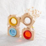 Conjunto de quatro blocos de madeira com janelas de cores diferentes: amarelo, azul, vermelho e transparente, empilhados com flores secas ao fundo.