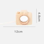 Câmara de madeira com lente circular e botão de ajuste, medindo 12cm de largura e 4,8cm de altura, usada como peça decorativa ou educativa.