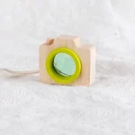 Câmara de brinquedo de madeira com lente verde, detalhes de madeira natural e cordão branco, sobre fundo branco.
