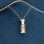 Colar com pingente de cilindro de vidro transparente, detalhes dourados e pequenas pedras, suspenso numa corrente fina de ouro.