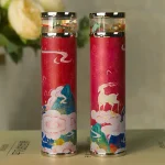 Duas varetas de incenso decorativas com embalagens coloridas e detalhes de animais e nuvens, colocadas em fundo neutro com flores ao fundo.