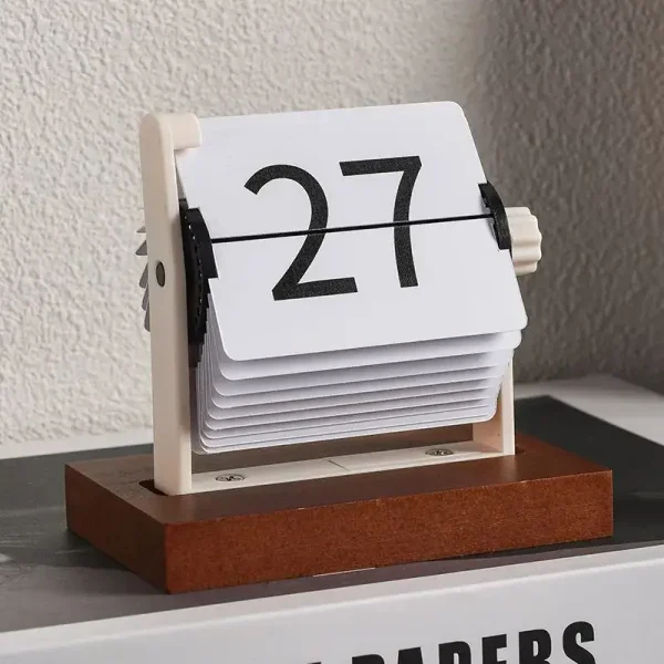 Calendário de mesa com números grandes em cartão rotativo, apoiado numa base de madeira, colocado numa superfície plana junto a uma parede texturizada.