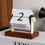 Relógio de calendário de mesa com mecanismo de rotação manual, exibindo o número 2, em acabamento de madeira e plástico.