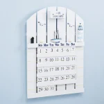 Calendário de parede de madeira branca com mês de janeiro, dias da semana e detalhes decorativos, incluindo pequenas figuras e uma vela.