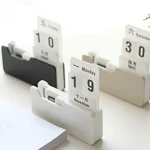 Calendário de mesa com blocos de dias, meses e anos em cores neutras, com fundo branco e luz natural.