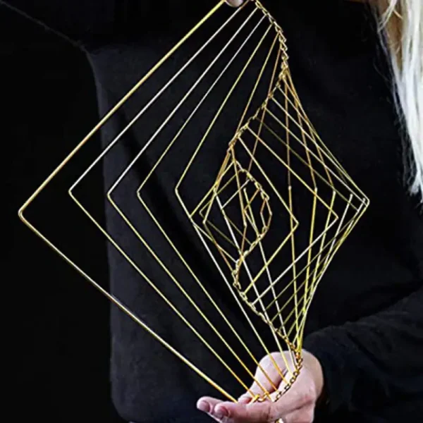 Escultura de fios dourados formando uma espiral geométrica, segurada por uma pessoa com roupa escura, fundo preto.