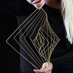 Escultura de arte geométrica feita de barras de metal dourado, com formas de quadrados e retângulos em diferentes tamanhos, segurada por uma pessoa com roupa preta.