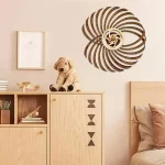 Arte decorativa em madeira com padrão espiral e detalhes em cores claras, colocada numa parede branca acima de um móvel de madeira clara com objetos decorativos e um cão de peluche.