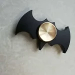 Fidget spinner com corpo de morcego em preto e rotação de metal dourado no centro.