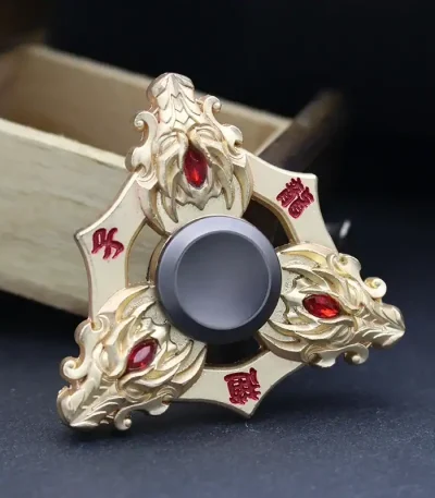 Fidget spinner decorativo com detalhes dourados e pedras vermelhas, visto de cima com fundo preto.