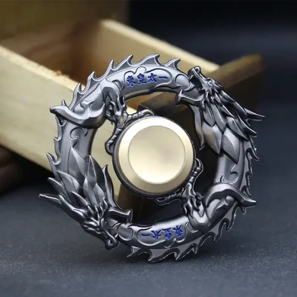 Peça decorativa de dragão em metal com detalhes em azul, forma circular, com escamas e cabeça de dragão, sobre fundo escuro e caixa de madeira ao lado.