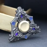 Fidget spinner metálico com detalhes decorativos em azul e roxo, visto de frente com foco no centro e nas extremidades.