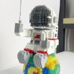 Figura de astronauta feita com blocos de construção, sentado sobre uma base colorida, segurando uma antena, com detalhes em preto, branco, vermelho, azul e amarelo.