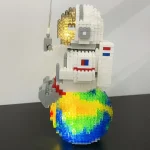 Estátua de astronauta feita com blocos de LEGO, segurando uma bandeira e uma ferramenta, com um planeta colorido na base.