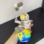 Estátua de LEGO de um astronauta com capacete dourado, segurando balão de balões de cores variadas, apoiada na mão de uma pessoa.