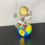 Estátua de astronauta feita com blocos de construção, sentado numa esfera colorida que representa o planeta Terra, com detalhes em dourado no capacete.