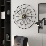 Relógio de parede com estrutura metálica preta em forma de geometria complexa, com ponteiros dourados, numa sala moderna com estante e cadeira de escritório.